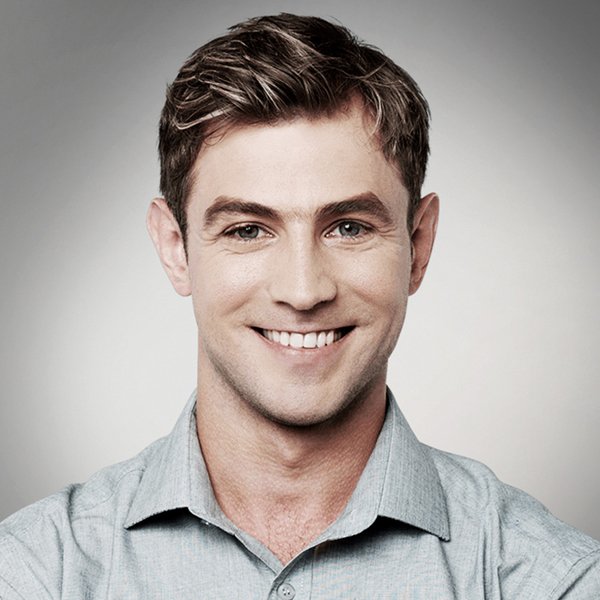 Man smiling, wearing a light blue button-down shirt, neutral background.