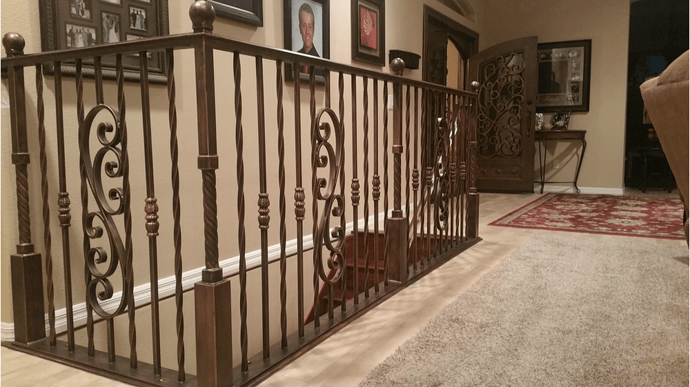 Brown wrought iron railing along a hallway with carpet, decorated walls, and a decorative door.