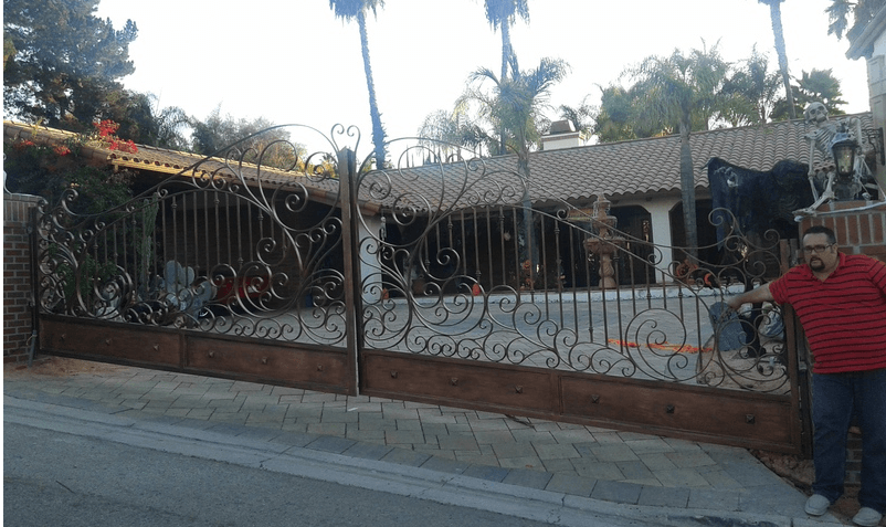 Man stands near ornate wrought iron gate in front of a house.