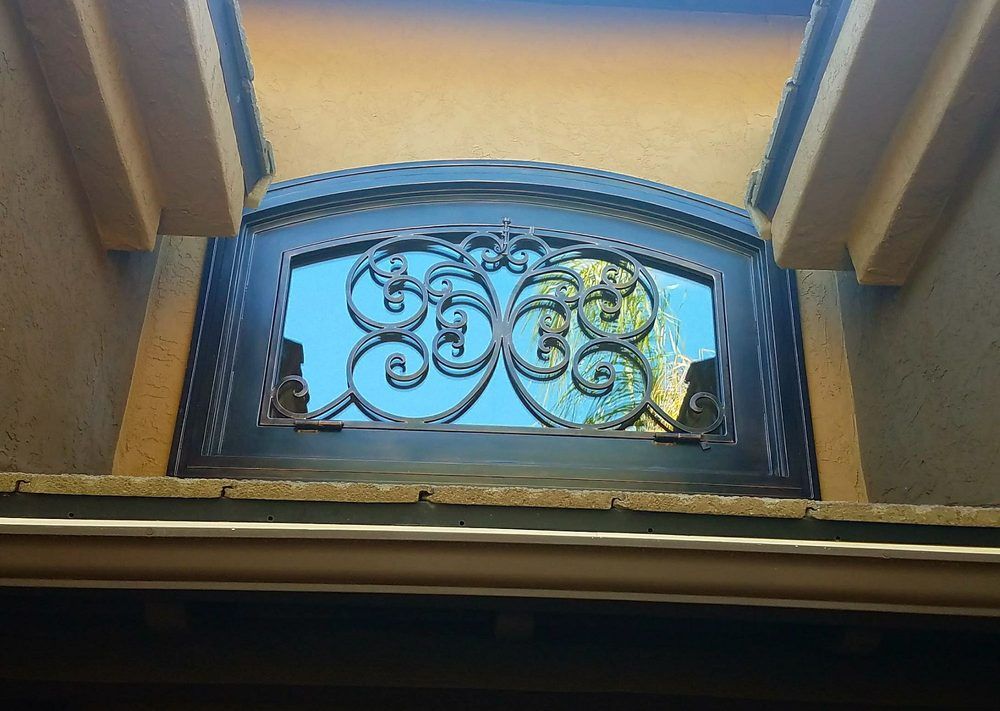 Black ornate metal window with arched top; blue sky visible.