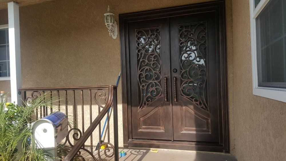 Brown double doors with decorative ironwork, on a porch with matching railing and mailbox.