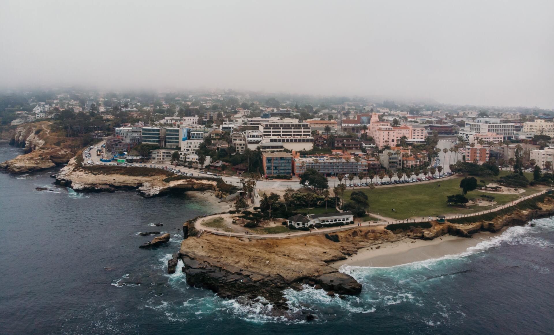 Coastal city view with ocean, cliffs, buildings, and a foggy sky.
