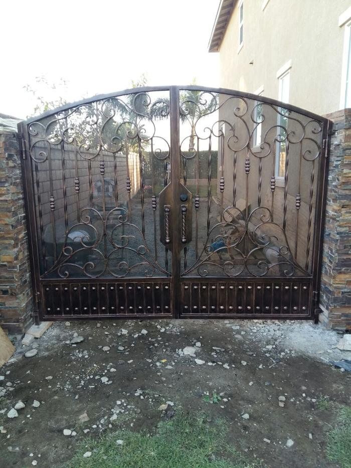 Ornate, dark brown wrought iron gate with stone pillars, arched top, and decorative scrollwork.